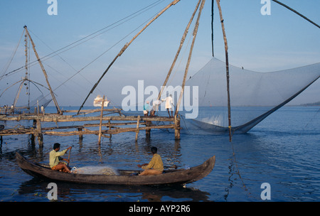 INDIA South Asia Kerala Kochi Cochin Chinese fishing net being raised with a catch as two men row past in a canoe Stock Photo