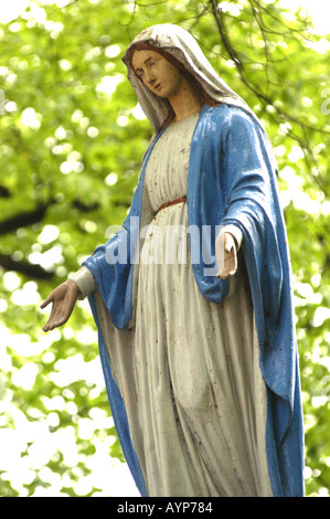 A statue of the Virgin Mary standing in a summer garden in black and ...