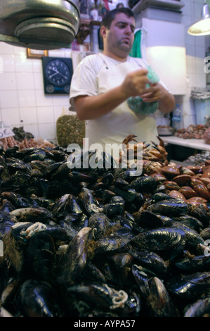 A fishmonger works behind a display of fresh mussels at the interiors of central market in Malaga Andalusia Spain. Stock Photo