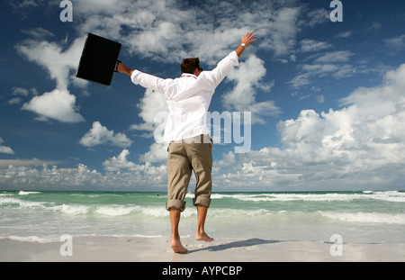 Businessman running and jumping on the beach with arms outstretched holding briefcase Stock Photo