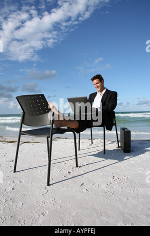 Young businessman sitting on a chair on the beach working on his laptop Stock Photo