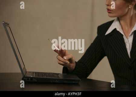 A businesswoman smoking with a laptop beside her Stock Photo