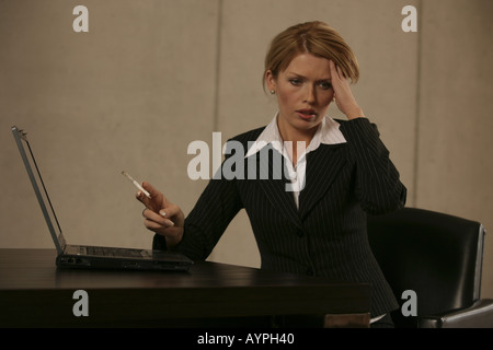 A businesswoman smoking with a laptop beside her Stock Photo