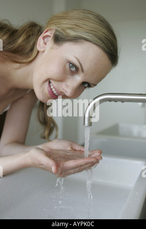 A blonde woman holds water in her palms as she smiles at the camera ...