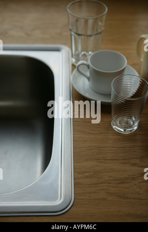 Two glasses cup and a saucer placed beside a steel sink Stock Photo