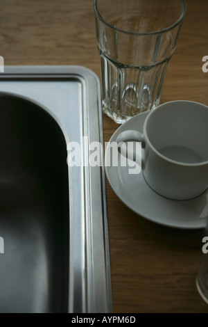 A glass cup and a saucer placed beside a steel sink Stock Photo