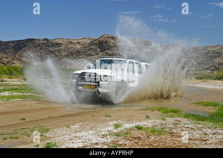 Off-road vehicle (4X4) driving through a large puddle in the otherwise dried-up Huanib River Valley, Kaokoveld, Namibia, Africa Stock Photo