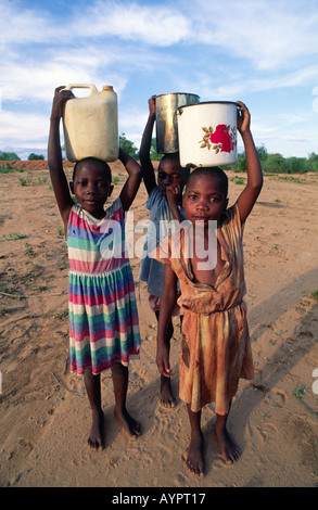 Young girls from the BaTonga tribe carrying water home on their heads from a well some distance away. Nr Binga, Zimbabwe Stock Photo