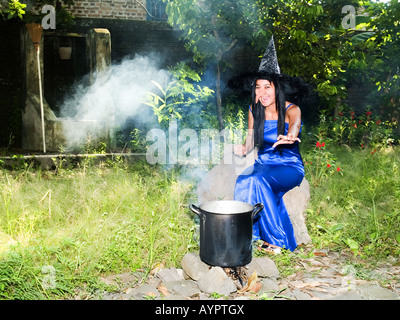 Young,pretty witch in blue dress and pointed hat casts spells in a garden,Madiun,East Java,Indonesia. Stock Photo