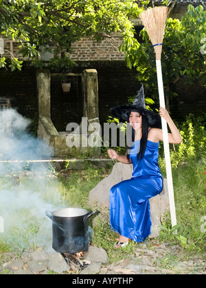 Young,pretty witch in blue dress and pointed hat casts spells in a garden,Madiun,East Java,Indonesia. Stock Photo