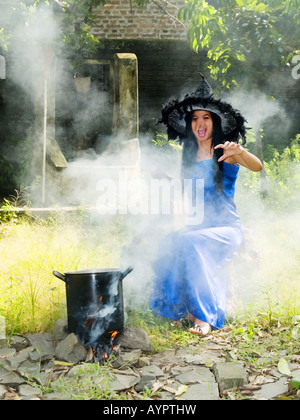 Young,pretty witch in blue dress and pointed hat casts spells in a garden,Madiun,East Java,Indonesia. Stock Photo