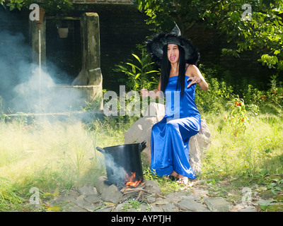 Young,pretty witch in blue dress and pointed hat casts spells in a garden,Madiun,East Java,Indonesia. Stock Photo