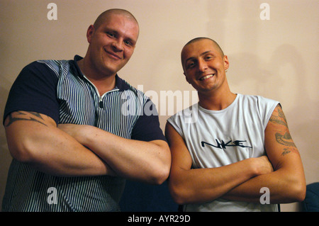Two strong men with folded arms, smiling and looking at the camera. Muscular men with tattoos and shaved heads posing together indoors. Stock Photo