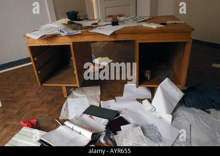 Total Mess in Old Fashioned Office with papers scattered across a wooden desk and floor, showing chaos, clutter, and signs of a ransacked room. Stock Photo