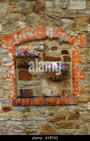 Window blocked by bricks and flowers on the Welsh countryside Swansea Wales UK. Rustic stone wall with decorative hanging floral baskets. Stock Photo
