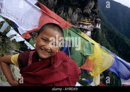 Portrait of a child monk in front of the Taktshang, also called Tiger Nest, the most impressive monastery of Bhutan Stock Photo