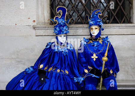 Two people wearing blue costumes and masks sitting on a bench in front of a window, Carnevale di Venezia, Carneval in Venice Stock Photo
