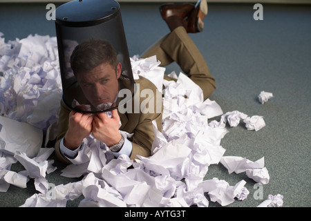 Businessman wearing a trash on head lying between crushed paper on floor Stock Photo