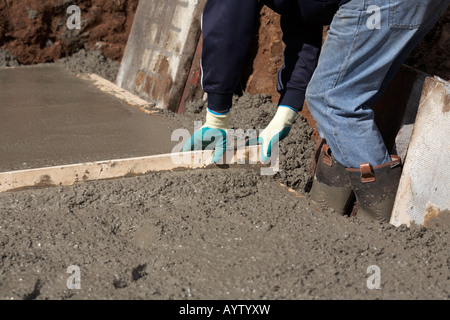 workman in protective boots and gloves uses piece of wood used to level off concrete whilst laying concrete base Stock Photo