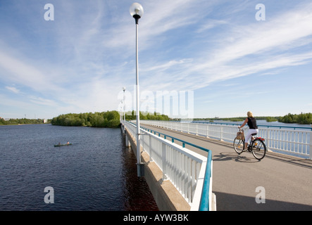 Woman cyclist on a bridge crossing River Oulujoki from Hietasaari islet to Korkiasaari islet and canoe at the river , Oulu Finland Stock Photo