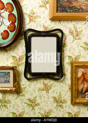 A blank frame hanging on a kitsch wall surrounded by other pictures Stock Photo