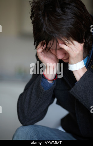 young dark haired teenage man sitting with his head in his hands staring at the floor Stock Photo