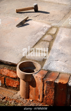 AN IMPROVISED PLANT POT MADE FROM A SECTION OF OLD CLAY SOIL PIPE BUILT INTO A PATIO LAID WITH NATURAL STONE SLABS UK Stock Photo
