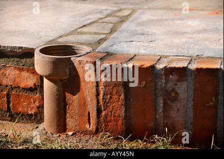 AN IMPROVISED PLANT POT MADE FROM A SECTION OF OLD CLAY SOIL PIPE BUILT INTO A PATIO LAID WITH NATURAL STONE SLABS UK Stock Photo