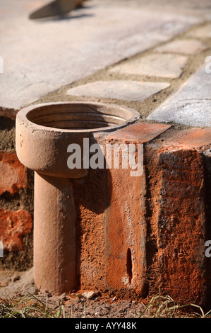 AN IMPROVISED PLANT POT MADE FROM A SECTION OF OLD CLAY SOIL PIPE BUILT INTO A PATIO LAID WITH NATURAL STONE SLABS UK Stock Photo