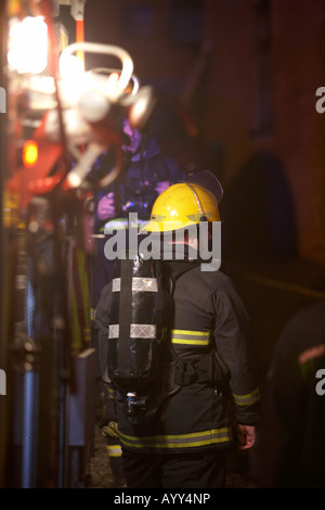 firefighter wearing breathing apparatus waits at the rear of a fire tender truck at the scene of a house fire in the uk Stock Photo