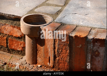 AN IMPROVISED PLANT POT MADE FROM A SECTION OF OLD CLAY SOIL PIPE BUILT INTO A PATIO LAID WITH NATURAL STONE SLABS UK Stock Photo