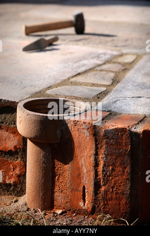 AN IMPROVISED PLANT POT MADE FROM A SECTION OF OLD CLAY SOIL PIPE BUILT INTO A PATIO LAID WITH NATURAL STONE SLABS UK Stock Photo