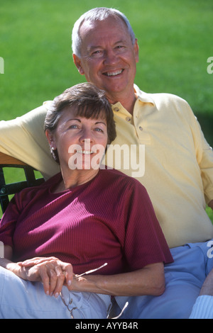 Happy, mature couple relax on a park bench on a beautiful spring or summer day. Stock Photo