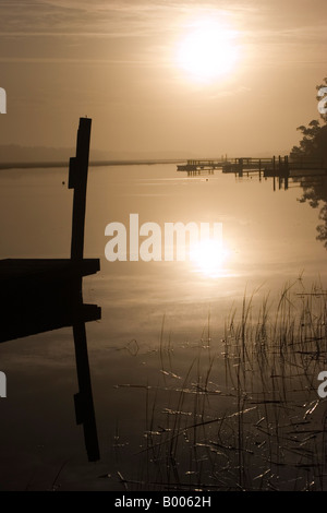 The early December morning sun rises through the mist behind a dock at Bald Head Creek in Bald Head Island, North Carolina. Stock Photo