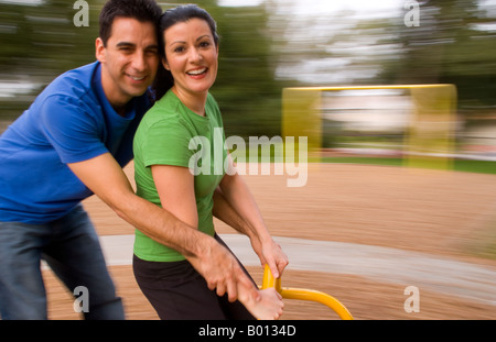 Couple in their 30s dating and having fun in playground spinning blurred on mary go round in park Stock Photo