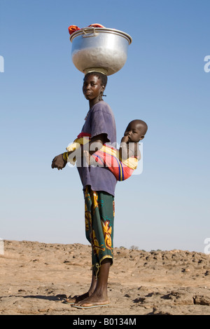 Mali, Dogon Country, Sangha. A woman returns home from washing clothes in a nearby river with her child slung on her back. Stock Photo