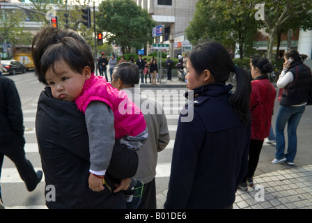 Exhausted child carried by mother through downtown crowds, Shanghai, China Stock Photo