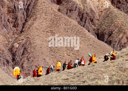a long line of monks is carrieng a huge Tanka up a maountain in Labrang monastery in Qinghai provice China Stock Photo