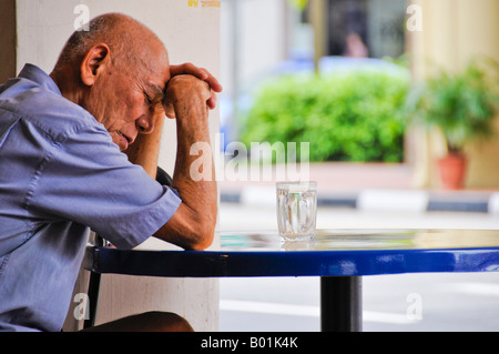 Older Asian man sitting down at empty table in restaurant in Singapore Stock Photo