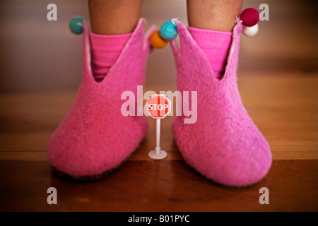 Girl aged four in pink felt slippers stands over small plastic toy stop sign Stock Photo