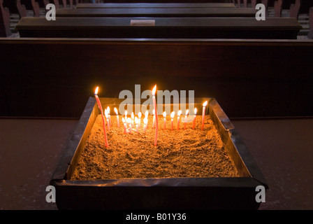 Horizontal close up of religious 'votive candles' alight inside a dark church. Stock Photo
