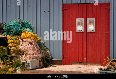 Red doors of a fishermans equipment shed with piles of tangled netting and rope coils outside Stock Photo