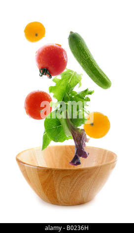 Assorted fresh vegetables falling into a wooden salad bowl isolated on white background Stock Photo
