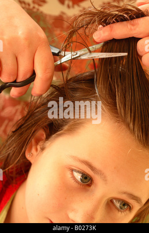 Young teenage girl aged 14 years having her long hair cut with scissors looking apprehensive Stock Photo