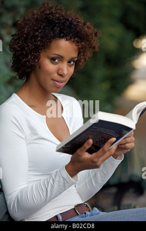 Afro-German girl - half German half Cuban - sits in a park and reads a book Stock Photo