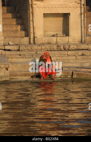 An Indian man dressed in red offers puja, prayers, on the banks of the Ganges river. Stock Photo