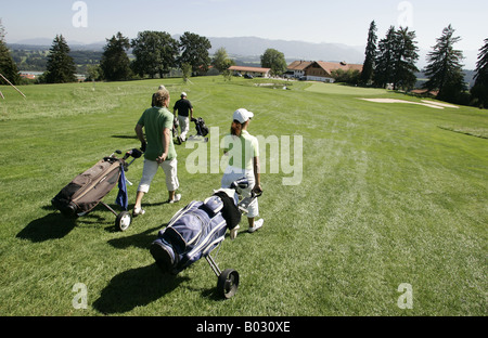 Flight of three golfers with golf carts on fairway in Gsteig,Bavaria approaching the clubhouse. Stock Photo