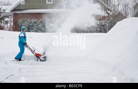 Woman with Electric Snowblower horizontal A woman in a blue snow suit uses an electric snow blower to clear a driveway