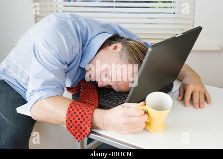 An stressed and exhausted businessman has fallen asleep on top of his laptop computer. Stock Photo