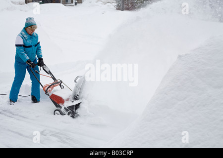 Woman with Electric Snowblower close A woman in a blue snow suit uses an electric snow blower to clear a driveway snowbank